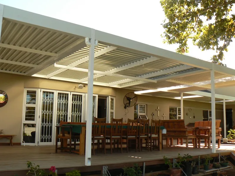White combination roof of solid and louvre panels over a timber deck with a long dining table