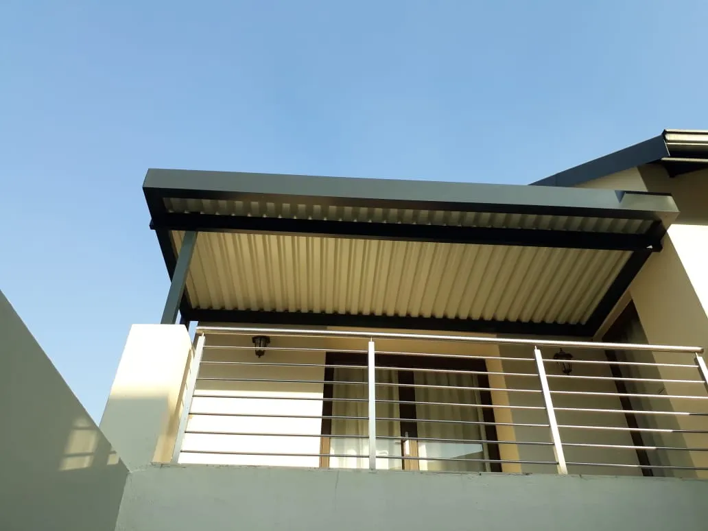 Charcoal-framed awning with a pale underside shading a first-floor balcony and its glass doors