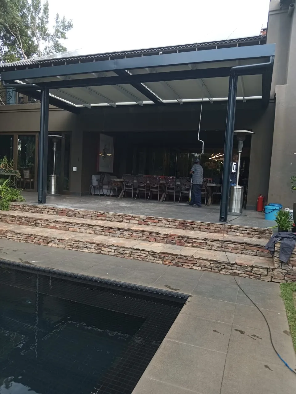 Charcoal-framed white louvre structure over a stone-stepped terrace and dark mosaic pool